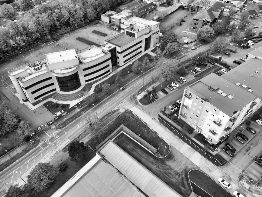 A black and white aerial photograph showing a modern multi-storey office building with a curved façade, situated on a street corner in Kingston town centre. The building is surrounded by a small land